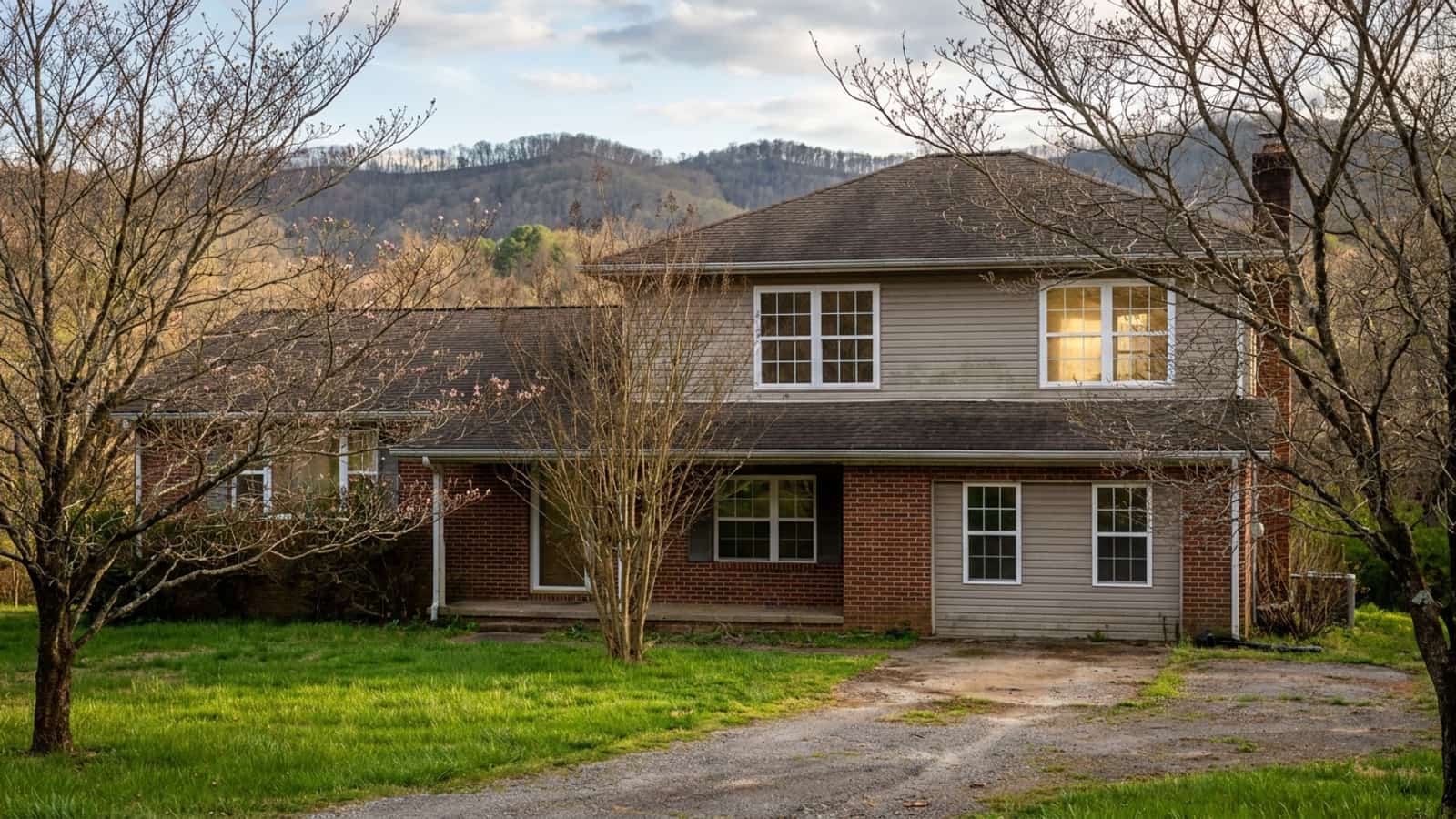 Two-story Southeastern home in early spring with bare dogwood trees and new white-framed windows catching afternoon light
