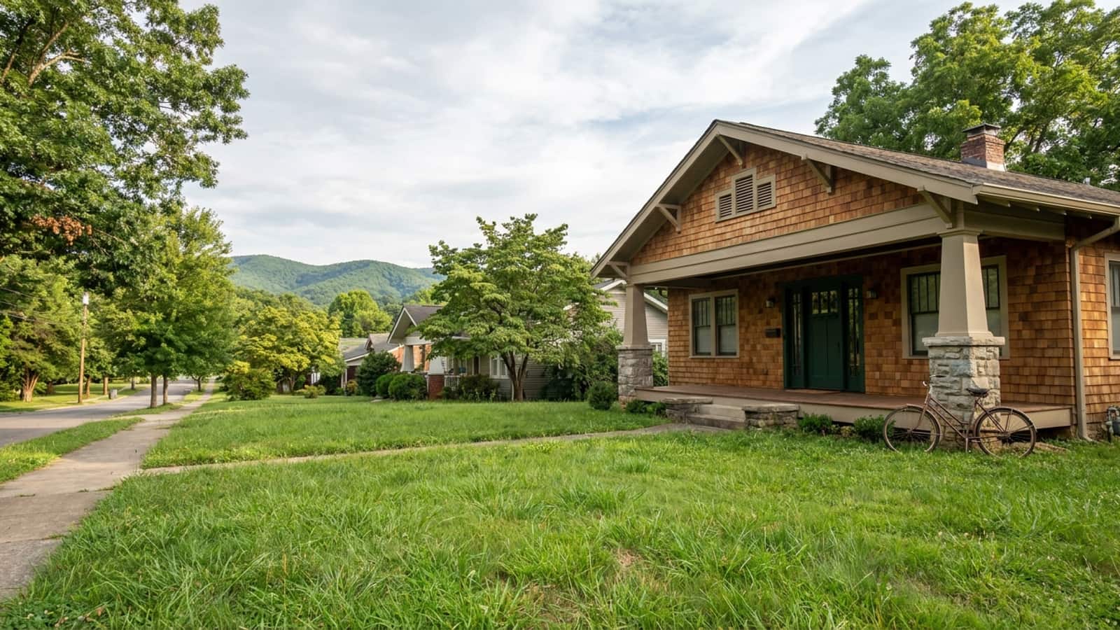 Craftsman bungalow with a covered front porch, tapered columns and a new dark green entry door with sidelights