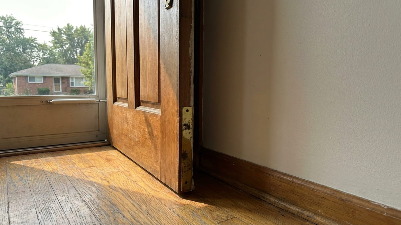 Wood entry door standing ajar with a visible gap at the top of the jamb and a scuffed strike plate