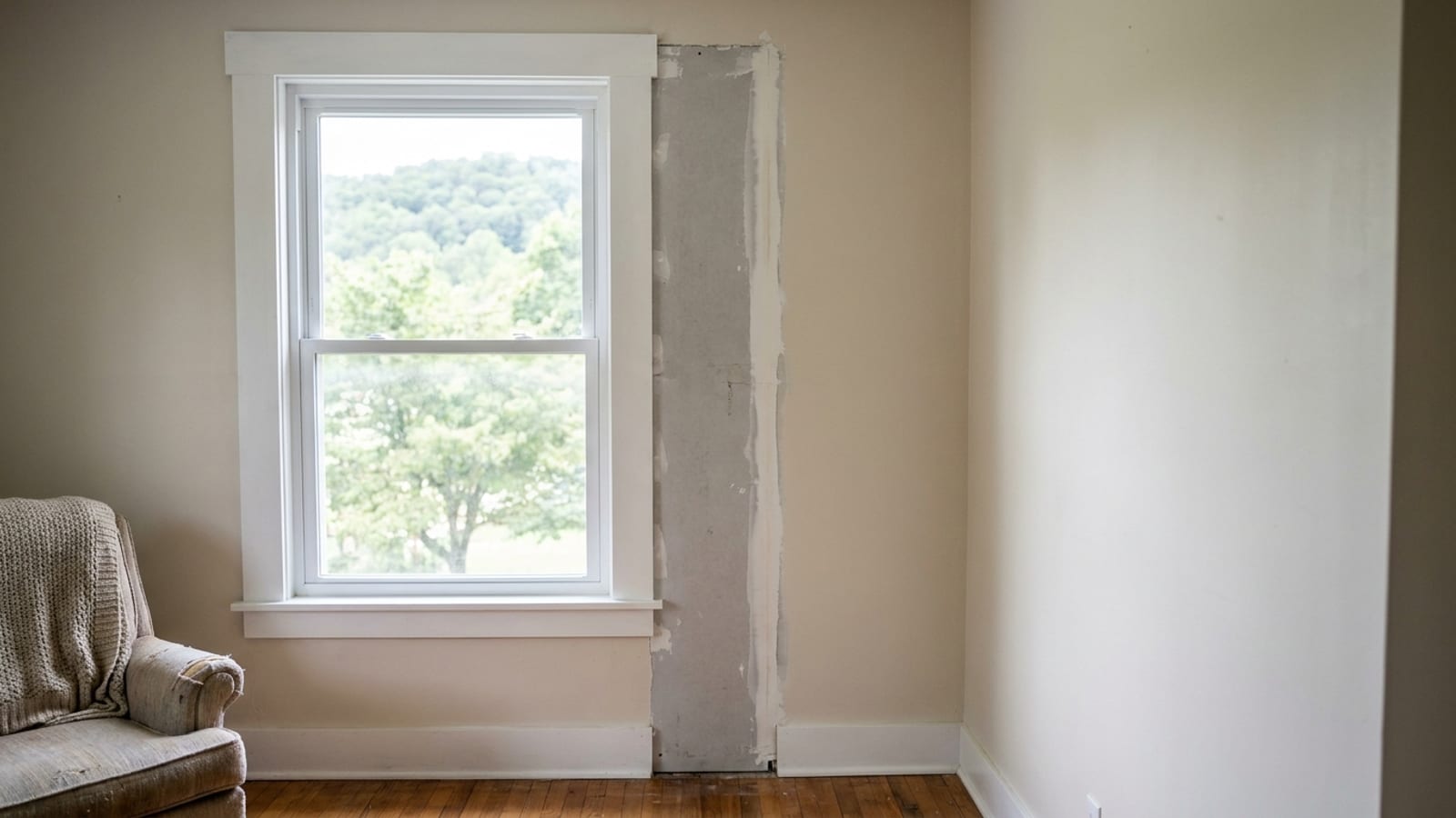 Interior corner of a living room with a newly installed white window, crisp painted casing and stool, and a small unfinished drywall edge beside it