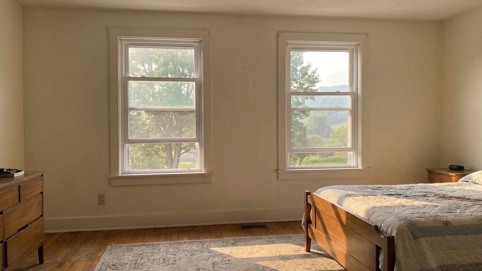 Two white vinyl windows side by side on a bedroom wall with morning light across a hardwood floor