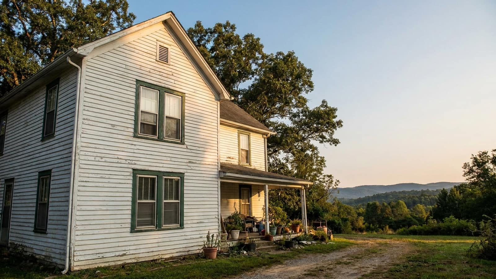 Older two-story clapboard home with aluminum storm windows over original wood sashes in late afternoon light