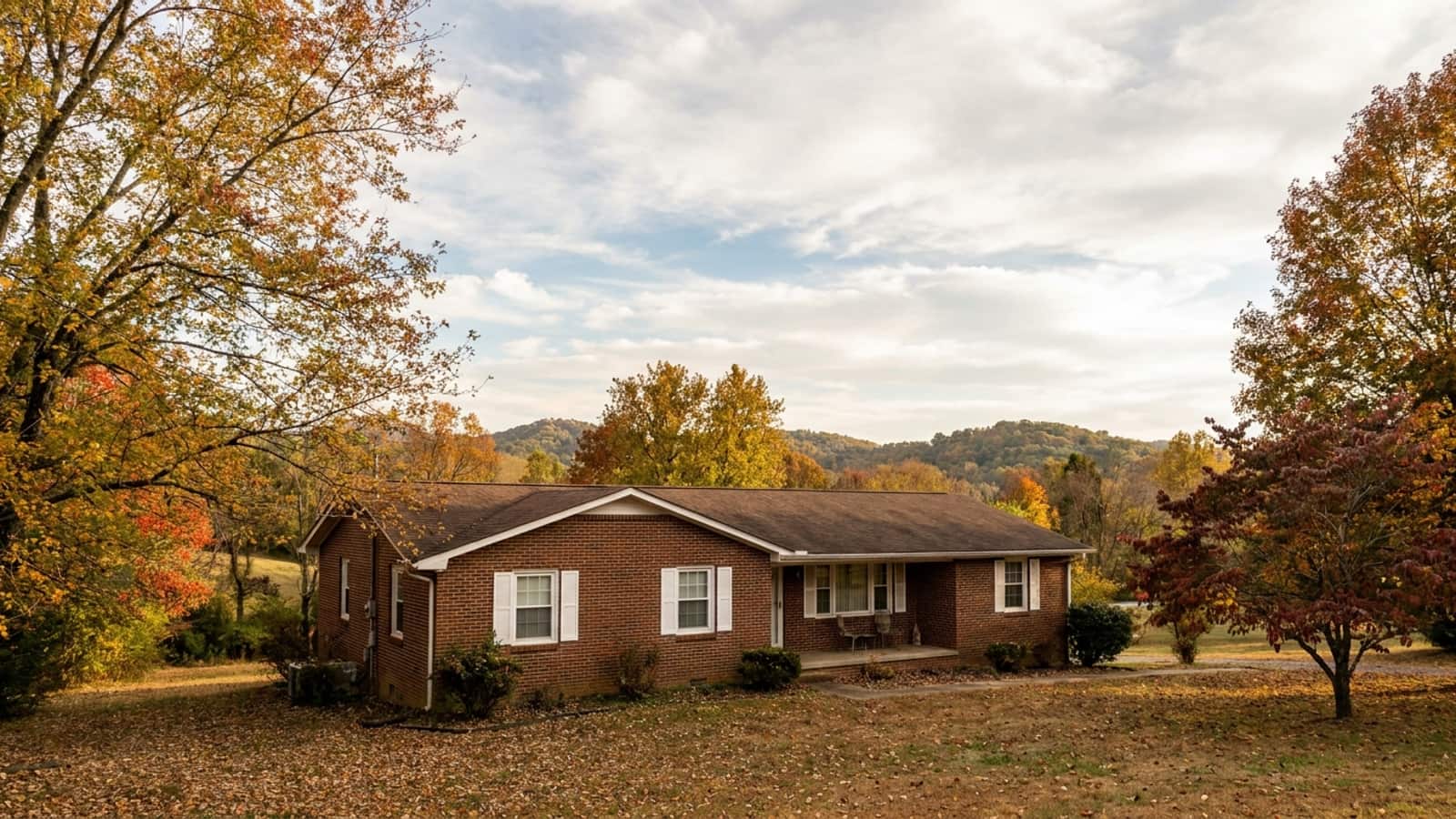 Brick ranch home in East Tennessee with white double-hung windows and autumn trees behind it